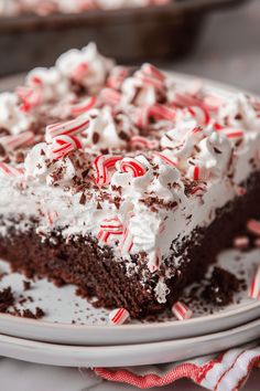 a slice of chocolate cake with white frosting and candy canes on top, sitting on a plate