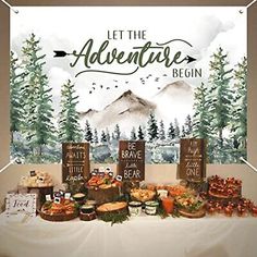 a table topped with lots of food next to a forest scene wall hanging on a wall