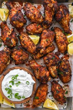 chicken wings with tzatzh and lemon wedges on a tray next to a small bowl of sour cream