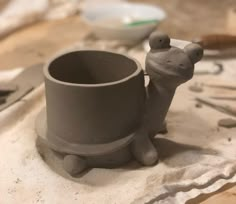 a clay cup with a small animal on it's side and some tools in the background