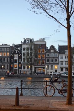 a bike parked next to a body of water with buildings in the background at dusk