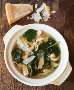 a bowl of soup with spinach, cheese and other food on a wooden table