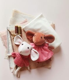 two stuffed animals are sitting on top of some cloths and other sewing supplies,