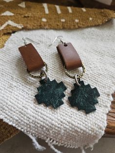 a pair of earrings sitting on top of a piece of fabric next to a pillow