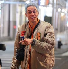 a man is walking down the street with his hand in his pocket and wearing an orange shirt