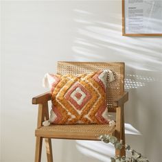 an orange and white pillow sitting on top of a wooden chair next to a plant