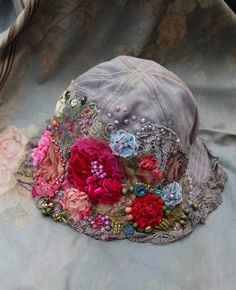 FleursBoheme original style hats '24. Romantic extravagant boho chic bucket hat is of denim fabric and hand dyed uneven light gray and beige shades. The large hand stitched/embroidered embellishments are made of various hand dyed vintage laces, textured velvet, silk, floral printed appliques, vintage trims. Accentuated with textile sculpted blossoms, hand stitches, various pearls, sequins, rich hand beading. Piece unique. Fits smaller size 54-56 cm; 21,2- 22 inches. Care: gently wash by hand in cool water. Boho Hat With Flowers, Bohemian Hats With Floral Embroidery And Curved Brim, Handmade Whimsical Summer Bucket Hat, Whimsical Handmade Bucket Hat For Spring, Adjustable Bohemian Hat With Floral Embroidery, Hippie Hat, Sequin Hat