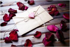 a piece of paper with a heart on it surrounded by rose petals and twine