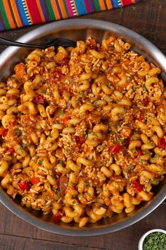 a bowl filled with pasta and sauce on top of a wooden table next to a striped napkin