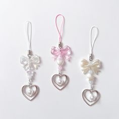 three heart shaped ornaments hanging from strings on a white surface, one with a bow and the other with pearls