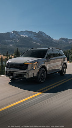 a silver suv driving down the road with mountains in the background