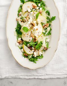 a white plate topped with green vegetables and feta cheese on top of lettuce