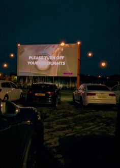 cars parked in front of a large screen at night