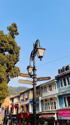 a street light with several signs on it in front of buildings and trees, under a blue sky