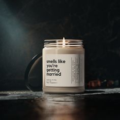 a candle sitting on top of a wooden table next to a black mug with the words smells like you're getting married written on it