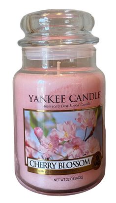 a pink candle with white flowers on the front and bottom, in a glass jar