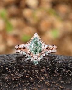 an engagement ring with a pear shaped green stone surrounded by small white diamonds on top of a rock