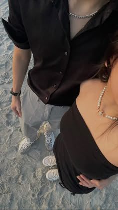 a man and woman standing next to each other on the beach with their hands around one another