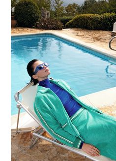 a woman laying in a lounge chair next to a swimming pool with her eyes closed