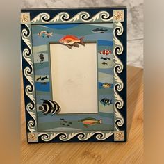 an artistic photo frame with fish and waves painted on the sides, sitting on a wooden surface