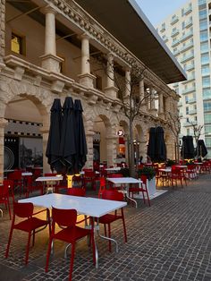 an outdoor dining area with red chairs and white tables, umbrellas on the roof