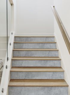 a set of concrete stairs leading up to a white wall and wooden handrails