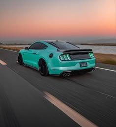 a turquoise mustang on the road at sunset