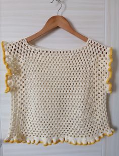 a crocheted top hanging on a wooden hanger next to a white wall