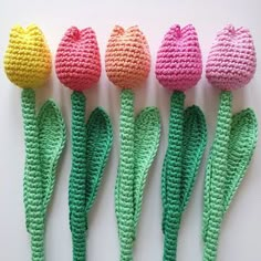 four crocheted tulips are lined up in a row on a white surface