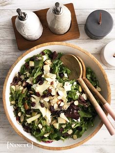 a white bowl filled with salad and wooden spoons next to two salt shakers