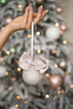 a woman's hand holding an ornament in front of a christmas tree