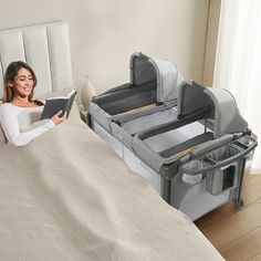 a woman laying in bed reading a book next to her baby crib and changing table