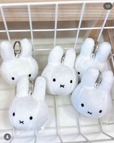 several white stuffed animals are on display in a wire rack with keychains attached to them