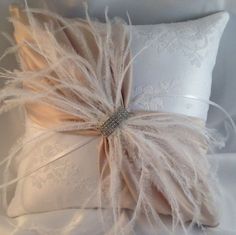 a white pillow with feathers on it and a ribbon around the edge, sitting on a bed