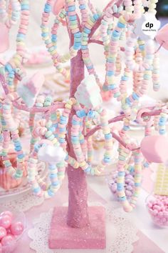 a pink and white table topped with lots of candy covered candies next to a tree