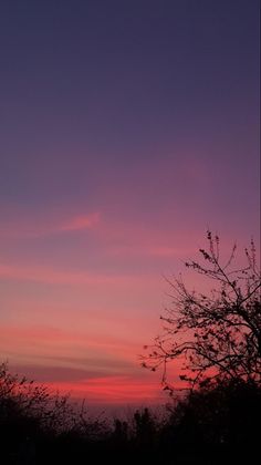 the sky is pink and purple as the sun sets in the distance with trees silhouetted against it