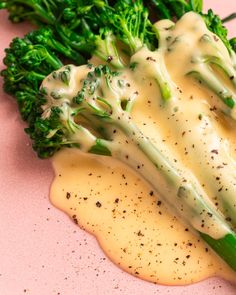 broccoli covered in white sauce on a pink surface