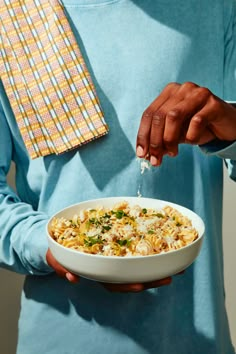 a man is holding a bowl of pasta and sprinkles with parsley