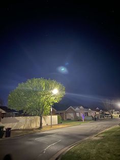 an empty street at night with the moon in the sky and trees on either side