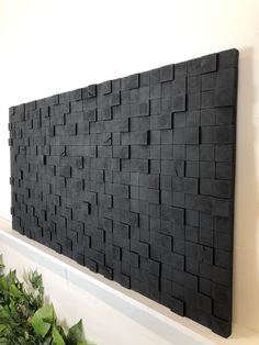 a black wall hanging on the side of a white wall with green plants in front of it