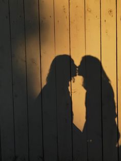 the shadow of two people kissing against a wooden wall