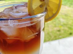 a drink with ice and lemon wedges on the rim next to a lawn area