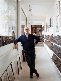 a man leaning against a wall in a room with many framed pictures on the walls