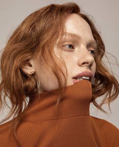 a woman with freckles on her hair is wearing an orange turtle neck sweater