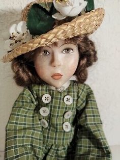 a doll wearing a hat with flowers on it's head and green plaid dress