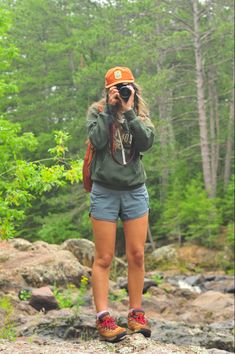 a woman standing on top of a rock while taking a photo with her cell phone