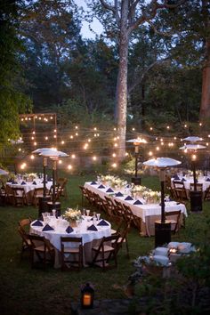 an outdoor dining area with tables and umbrellas lit up at night, surrounded by trees