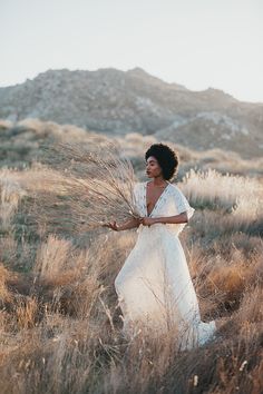 a woman in a white dress is walking through tall grass