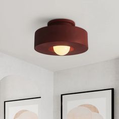 two framed pictures on the wall next to a red light fixture in a white room