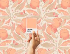 a hand holding up a pantone paint swatch in front of a floral wallpaper